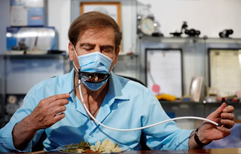 Meir Gitelis, co-développeur d'une société israélienne, mange tout en portant un masque muni d'une bouche mécanique qui s'ouvre pour permettre aux convives de manger sans l'enlever, comme les restrictions de la maladie du coronavirus (COVID-19) se relâchent, chez Avtipus Brevets et Inventions laboratoire à Or Yehuda, Israël 18 mai 2020 (crédit photo: AMIR COHEN / REUTERS)