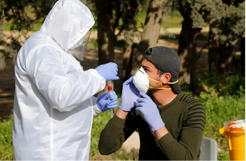Un membre du personnel médical échange un travailleur palestinien contre un test de la maladie à coronavirus (COVID-19), à son retour d'Israël, à l'extérieur du point de contrôle de Tarqumiya sous contrôle israélien, près d'Hébron, en Cisjordanie occupée par Israël le 26 mars 2020 (crédit photo: MUSSA QAWASMA / REUTERS)