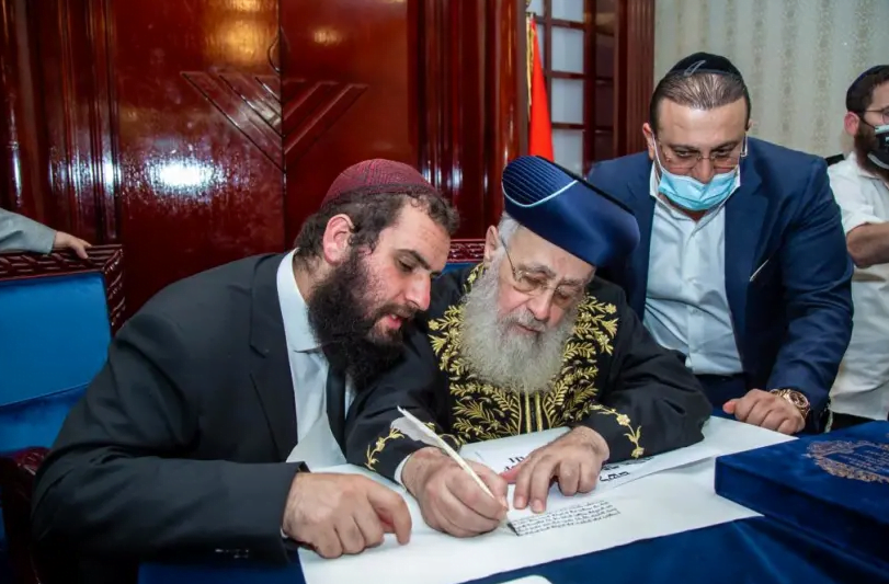Le grand rabbin israélien Yitzhak Yosef, au centre, écrit une partie d'un rouleau de la Torah au centre communautaire juif de Dubaï, le 19 décembre 2020. À gauche se trouve le chef du centre, le rabbin Levi Duchman. (crédit photo: GRÂCE AU CENTRE COMMUNAUTAIRE JUIF DE DUBAÏ)